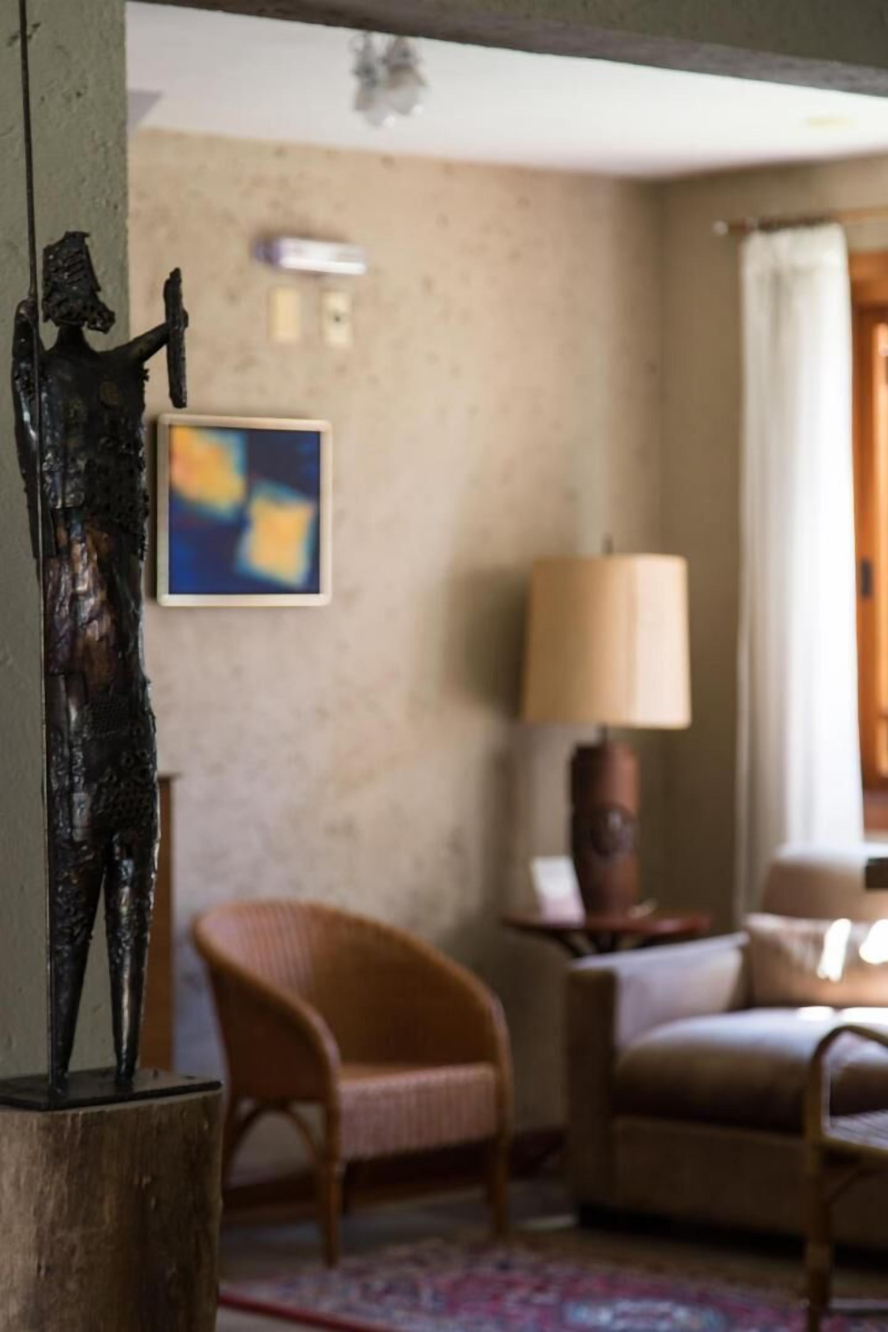 A room with a sofa, a chair, a lamp, and a wall-mounted artwork.