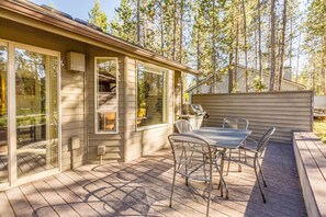 A covered patio with a table and chairs, a grill, and a view of a forested area. - Kinglet 28 (Bend)