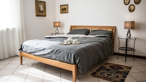 Un llit ben arropat amb un llençol gris, dues taules de nit amb làmpades i una catifa estampada sobre un terra de rajola.