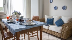 Zona de dinar amb taula preparada per l'esmorzar, un sofà de vimetla i un radiador.