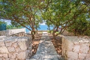 Un sendero de piedra que conduce a una vista panorámica del mar, bordeado por árboles y muros de piedra.