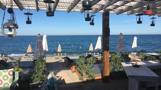 Eine Terrasse am Strand mit Sitzgelegenheiten, Sonnenschirmen und Blick auf das Meer.