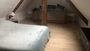 A bedroom with a sloped ceiling, a bed with a grey bedspread, a nightstand with a lamp, and a dresser. - THE THIRD RIVER OF ORNANS (Ornans)