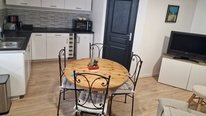 A compact kitchen with white cabinets, a black countertop, and a microwave. There's a dining table with metal chairs and a small cactus decoration. A dark door and a framed picture are on the wall. - THE THIRD RIVER OF ORNANS (Ornans)