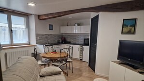 A cozy living area with a sofa, a round wooden dining table, and a television on a cabinet. - THE THIRD RIVER OF ORNANS (Ornans)