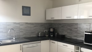 A modern kitchen with white cabinets, a black countertop, a dishwasher, a coffee maker, and a microwave. - THE THIRD RIVER OF ORNANS (Ornans)