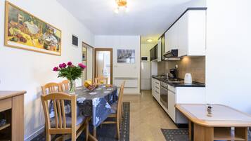 Una cocina compacta con electrodomésticos modernos, un comedor con mesa para dos personas y un cuadro en la pared.