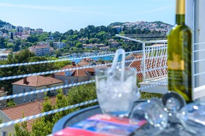 Un balcone con tavolo apparecchiato per mangiare, con vista su una cittadina costiera e imbarcazioni.