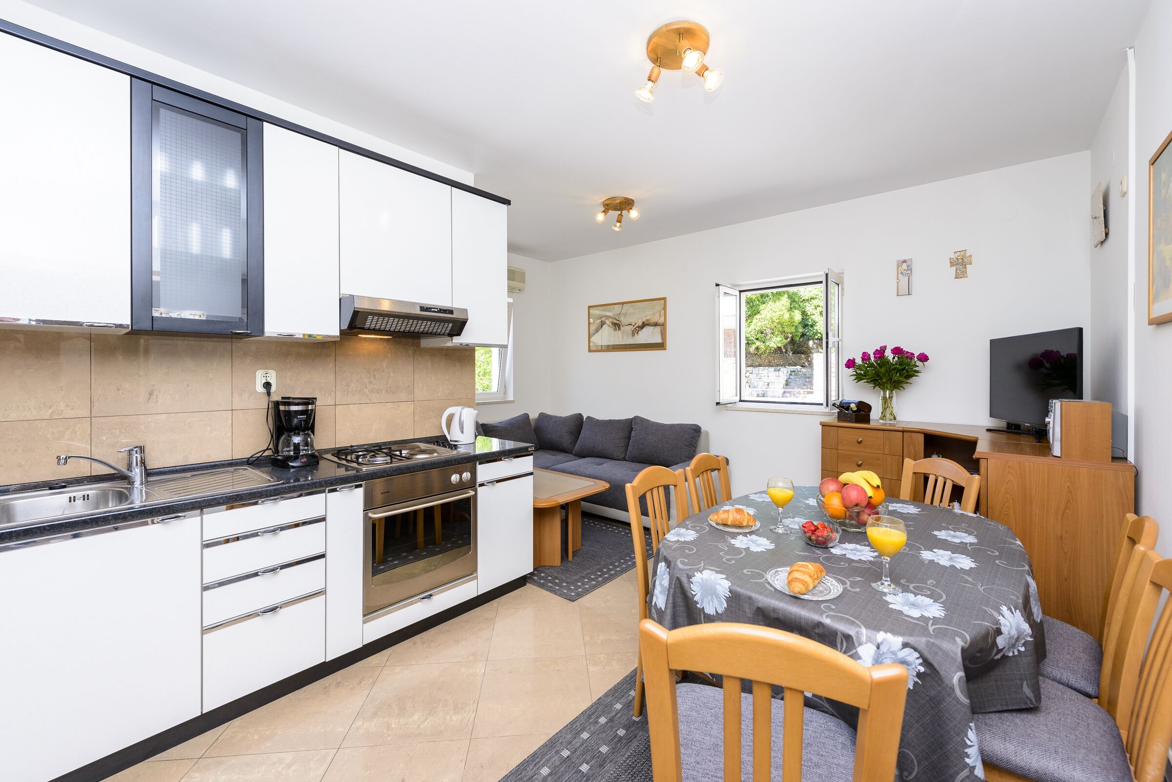 Cocina compacta con estufa, fregadero y microondas. Hay una mesa de comedor con sillas y un sofá en la sala.