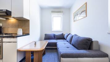 Un espacio habitable compacto con kitchenette, un sofá, una mesita y una ventana que proporciona luz natural.
