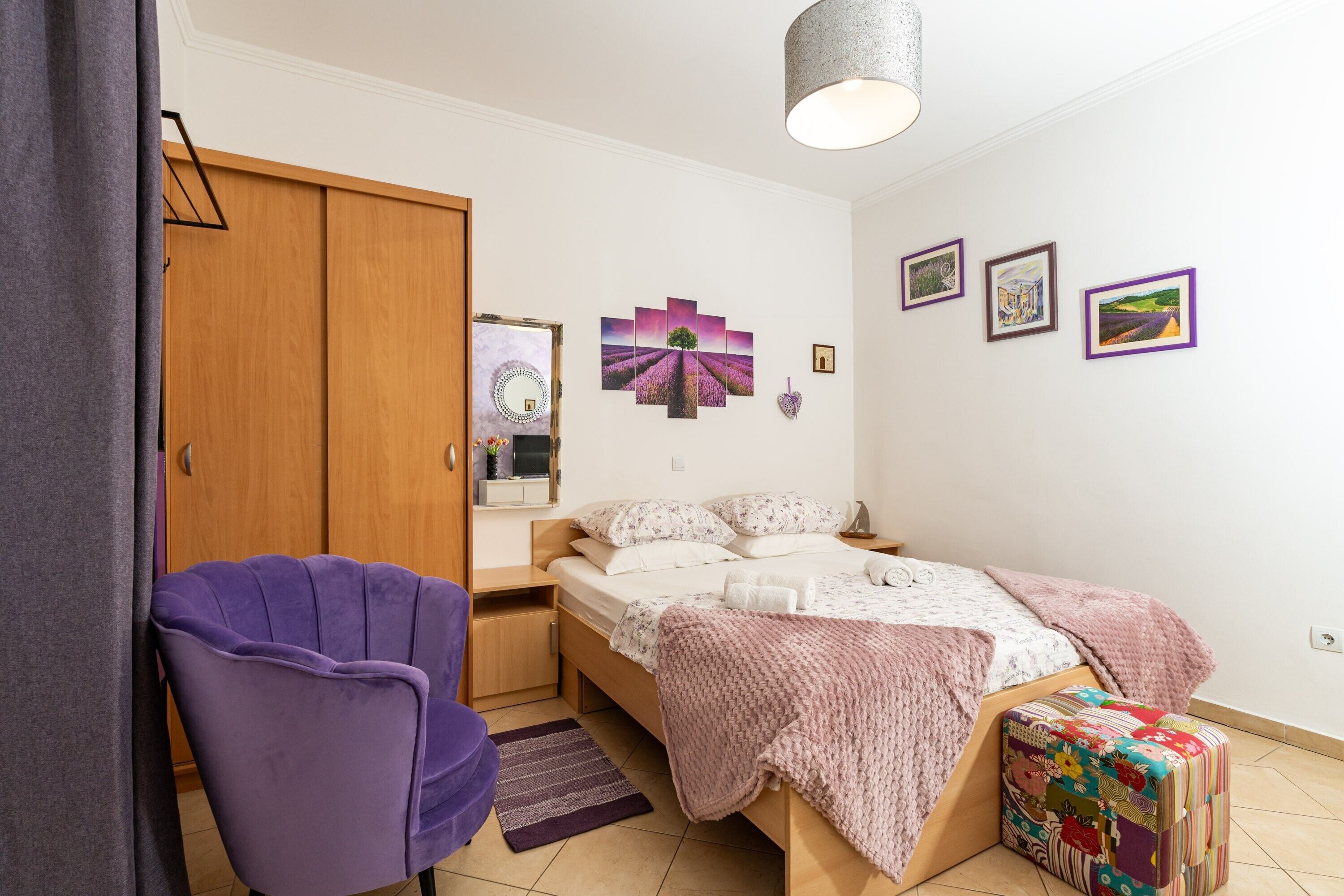 A bedroom with a bed, a purple chair, a wooden wardrobe, and a small table.