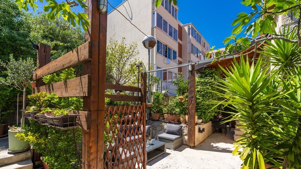 Eine Terrasse mit Sitzgelegenheiten im Freien, Kübelpflanzen und einem Holztor.