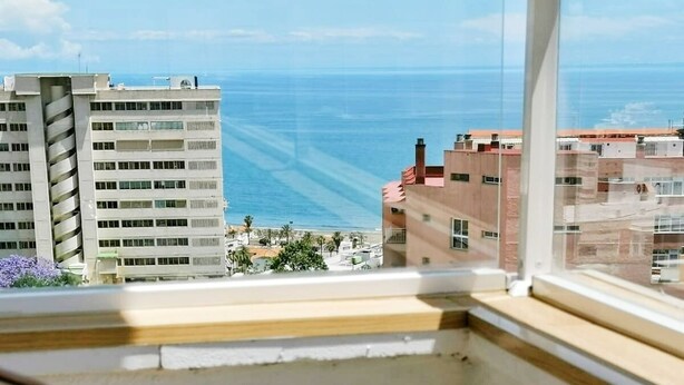 Un balcón con vista al mar, una copa de vino y una pequeña planta.