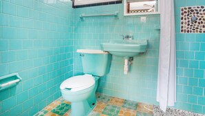 Un baño con azulejos turquesa, inodoro blanco, lavamanos y espejo.