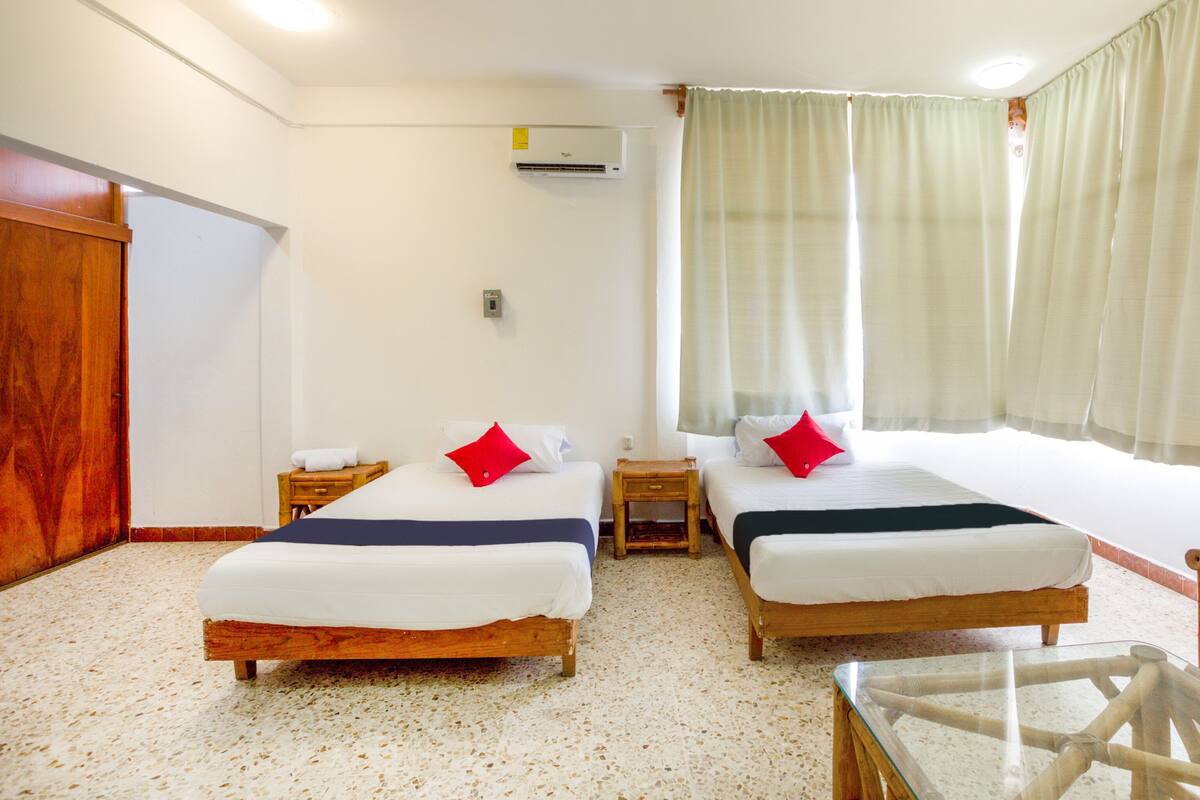 Habitació d'hotel amb dos llits, un armari de fusta, una taula petita i una taula de vidre.