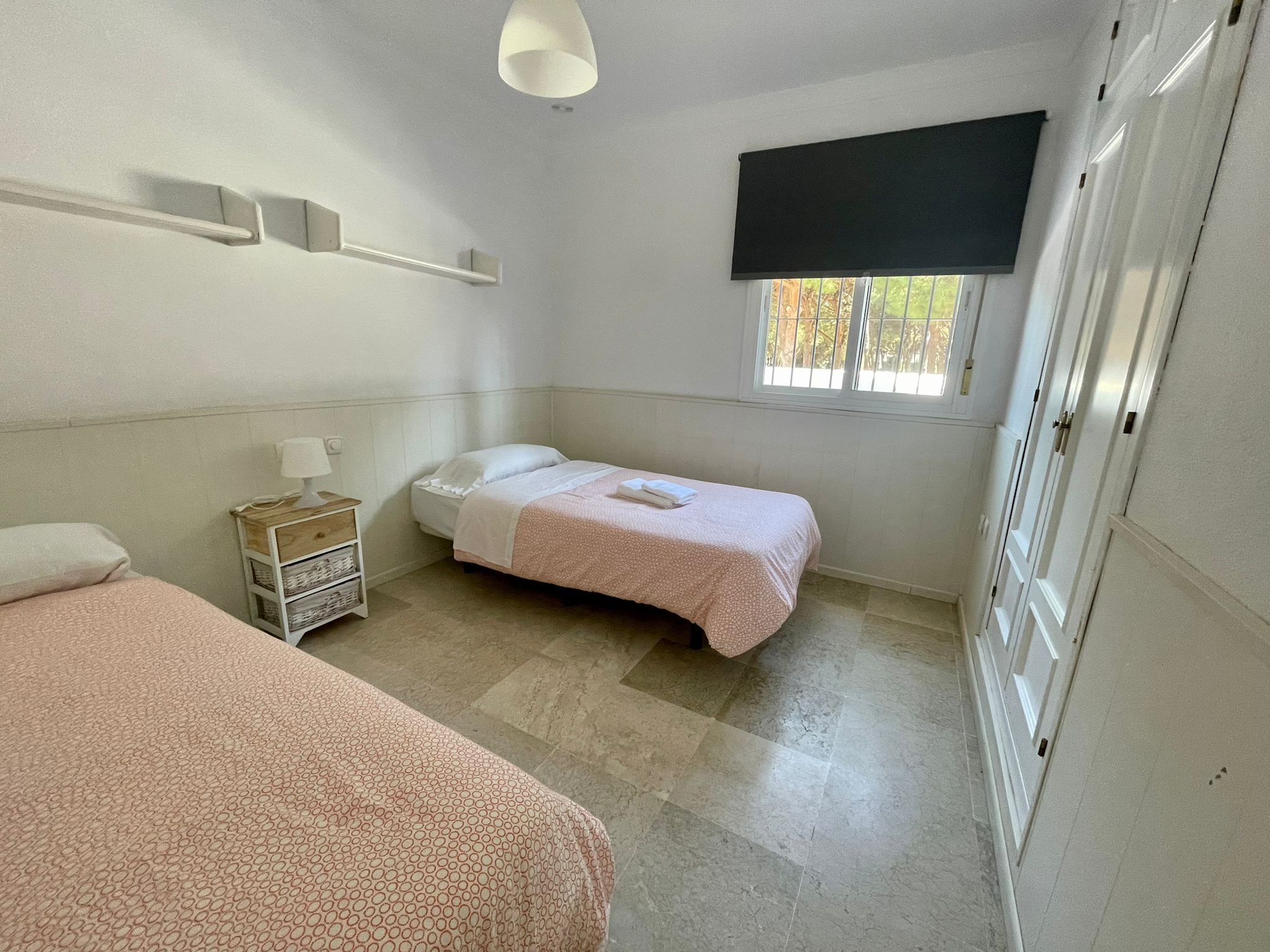 A bedroom with two beds, a nightstand, a window with a view, and a TV mounted on the wall.