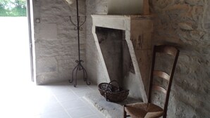 A stone-walled room with a fireplace, a chair, and a metal coat rack with a hat.