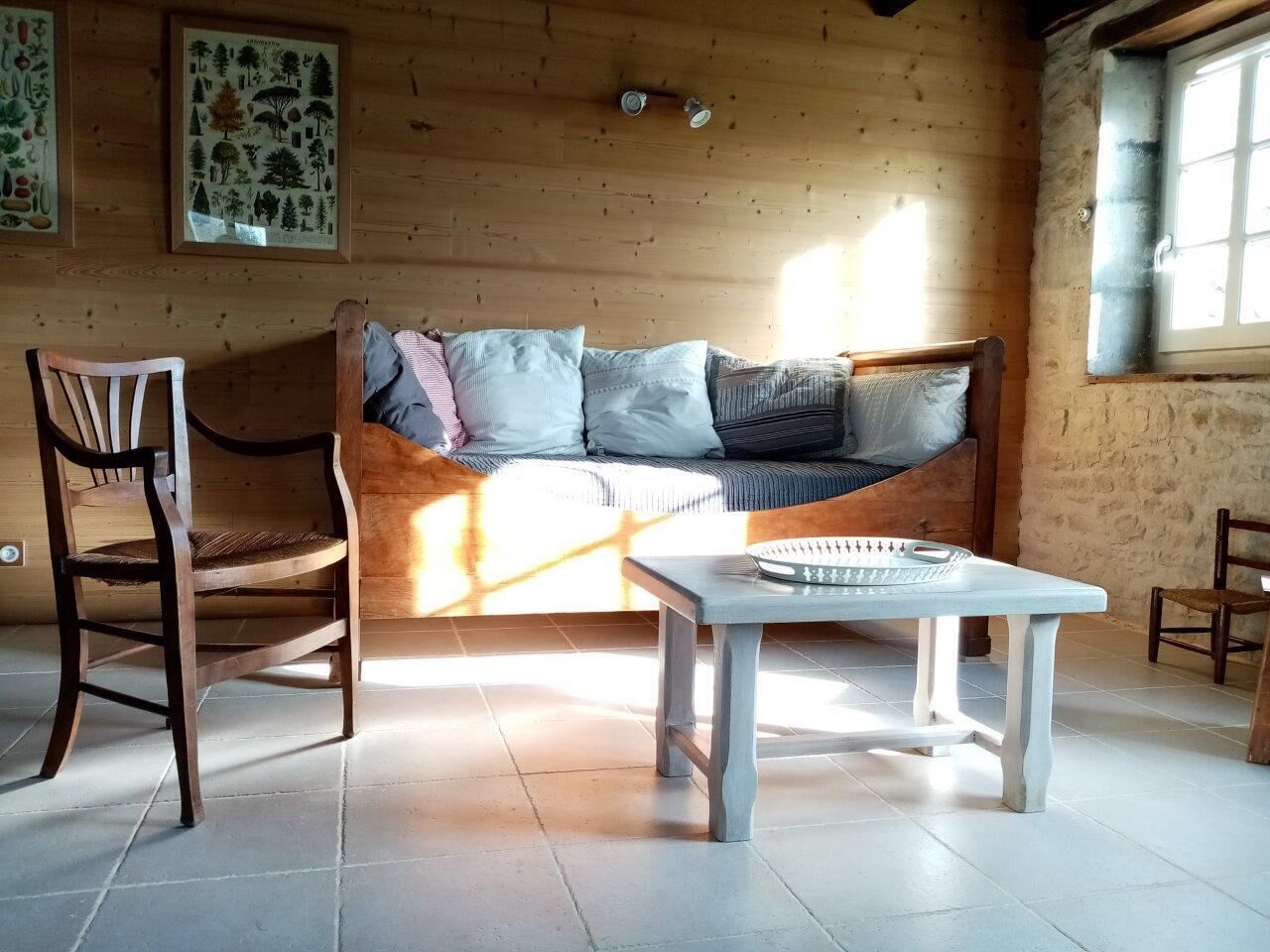 Tunnelmallinen huone, jossa on puuseinä, tyynyillä varustettu sohva, puinen tuoli ja pieni pöytä, jonka päällä on shakkilauta.