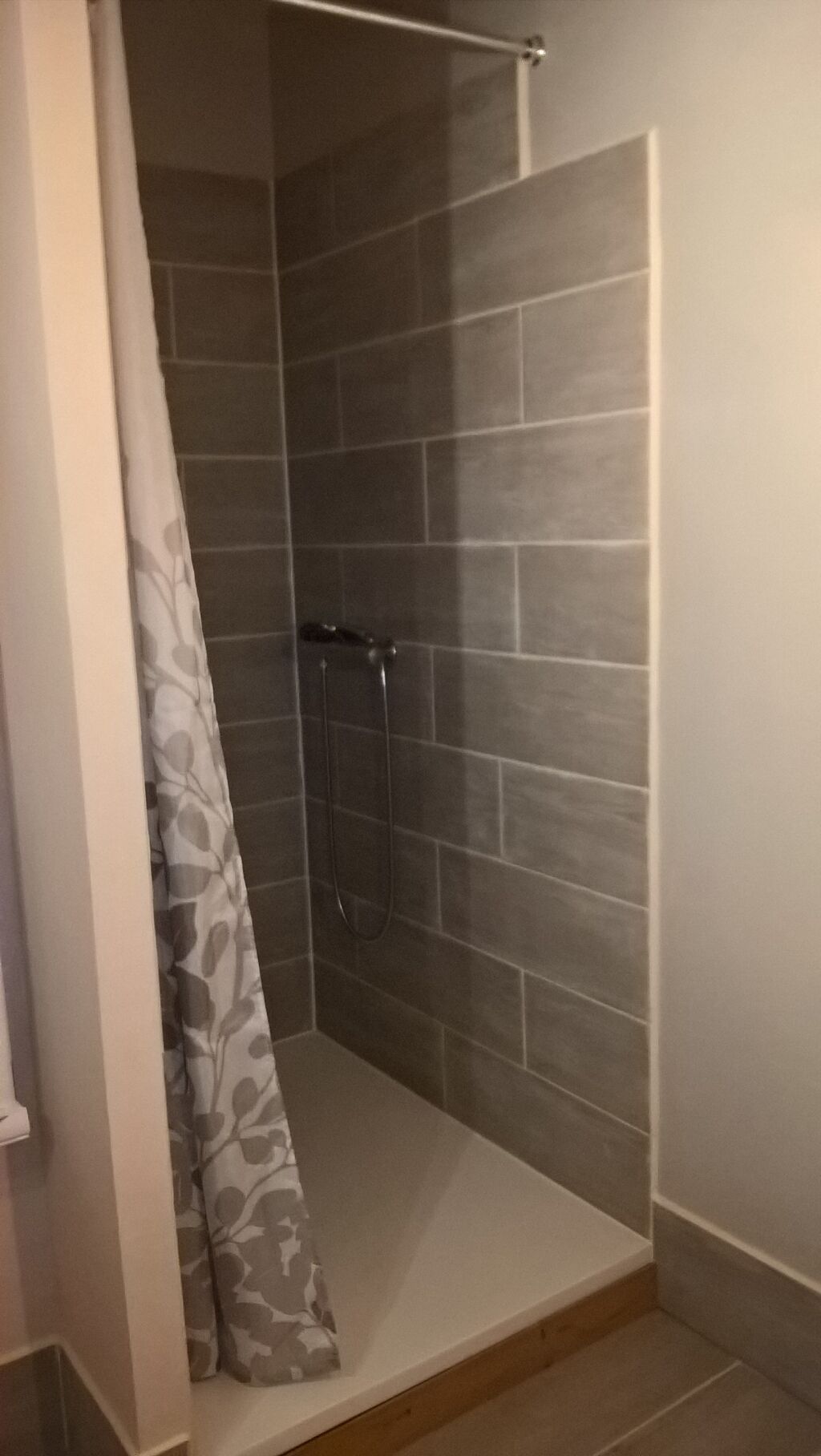 Eine Dusche mit grauen Fliesen und einer Duschvorhang.