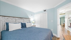 A bedroom with a bed, a nightstand, a wardrobe, and a door leading to another room. - Seacrest ~ Beach Front Condo (Gulf Shores)