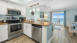 A modern kitchen with stainless steel appliances, a dishwasher, and a dining area with a view. - Seacrest ~ Beach Front Condo (Gulf Shores)