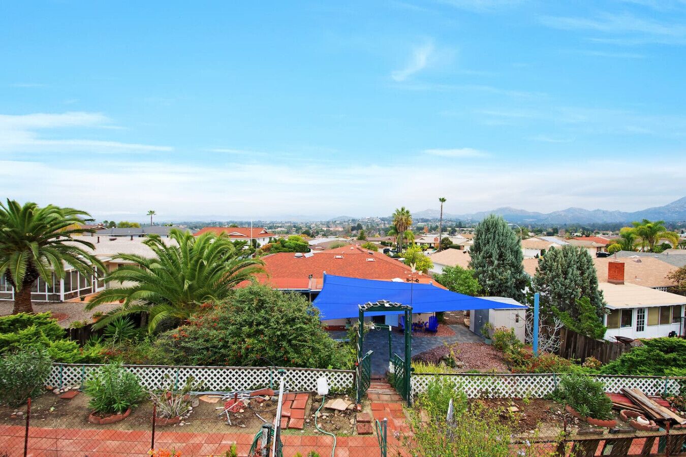 A residential area with a blue-roofed structure, a white fence, and various plants.