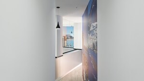A modern hallway with a view of a cityscape through a window, a pendant light, and a large poster on the wall.