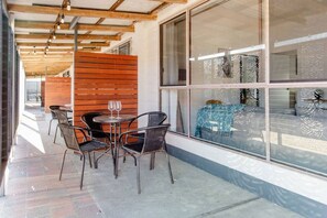 An outdoor seating area with a table and chairs, a wooden partition, and a view through large windows.