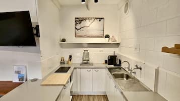 A compact kitchen with white cabinetry, a central island, a built-in stove, and a wall-mounted TV.