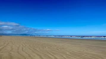 A wide sandy beach with gentle waves and a clear blue sky.