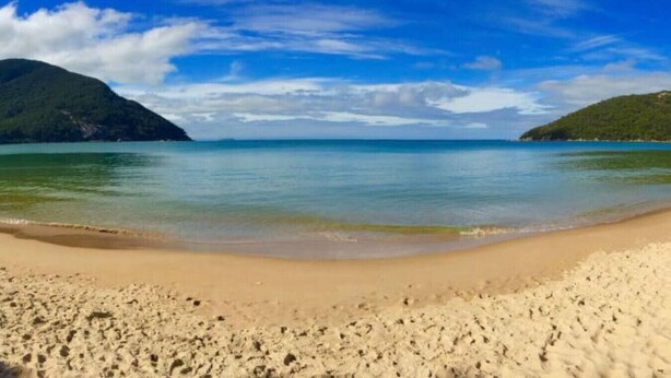 A beach with clear water, sandy shore, and distant green hills. - Prom Coast 4~ Slice of Paradise ~ Stunning Beach! (Sandy Point)