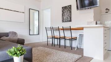 Un soggiorno moderno con un divano grigio, un tavolino da caffè con una pianta, una zona pranzo con sedie e tavolo, e un angolo cucina con una TV.
