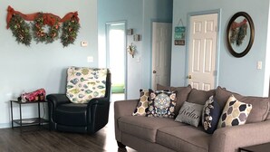 Een woonkamer met een bruine bank, een zwarte fauteuil en een houten vloer. Er is een deur met een krans aan de muur.