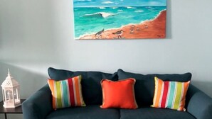 Een donkerblauwe bank met kleurrijke gestreepte kussens, een schilderij van een strandtafereel en een witte lantaarn op een tafel.