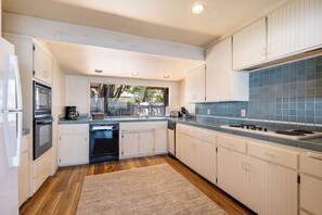 A modern kitchen with white cabinetry, a blue tiled backsplash, and a wooden floor. - Welcome to Titus Point! Breathtaking Oceanfront Escape with Panoramic Views! (Cambria)
