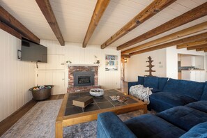 A living room with a fireplace, blue sofa, and a television mounted on the wall. - Welcome to Titus Point! Breathtaking Oceanfront Escape with Panoramic Views! (Cambria)