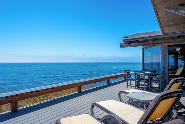 Una terraza de madera con mobiliario exterior que da a un mar azul y transparente.