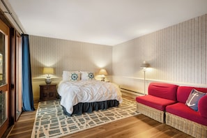 A hotel room with a bed, a red sofa, a patterned rug, and a wall with vertical lines.