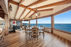 Un interior de madera con zona de comedor, ventanas amplias y vistas al mar.