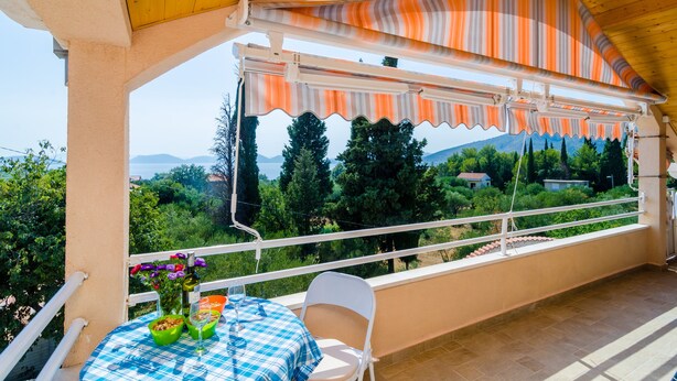 Un balcón exterior con mesa, sillas y vistas del paisaje.