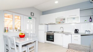 Una cocina compacta con armarios blancos, una mesa de comedor con sillas, un frutero rojo y un horno empotrado.
