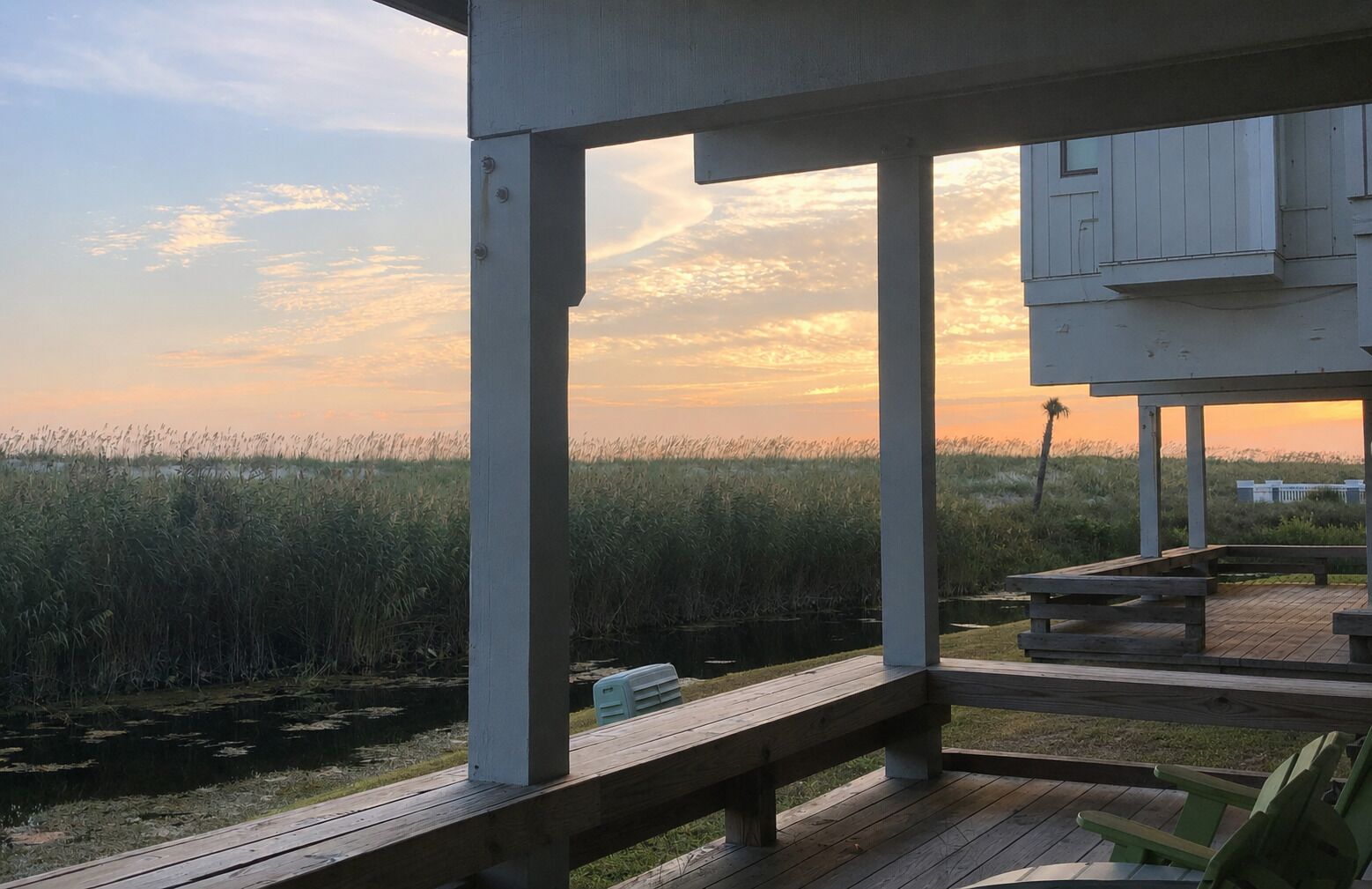 A wooden deck with a view of a marshy landscape and a sunset.