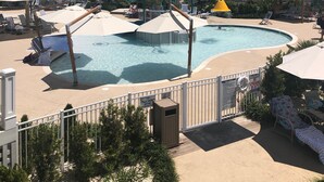 Ein Swimmingpool mit Liegestühlen und Sonnenschirmen, umgeben von einer Hecke und Pflanzen.