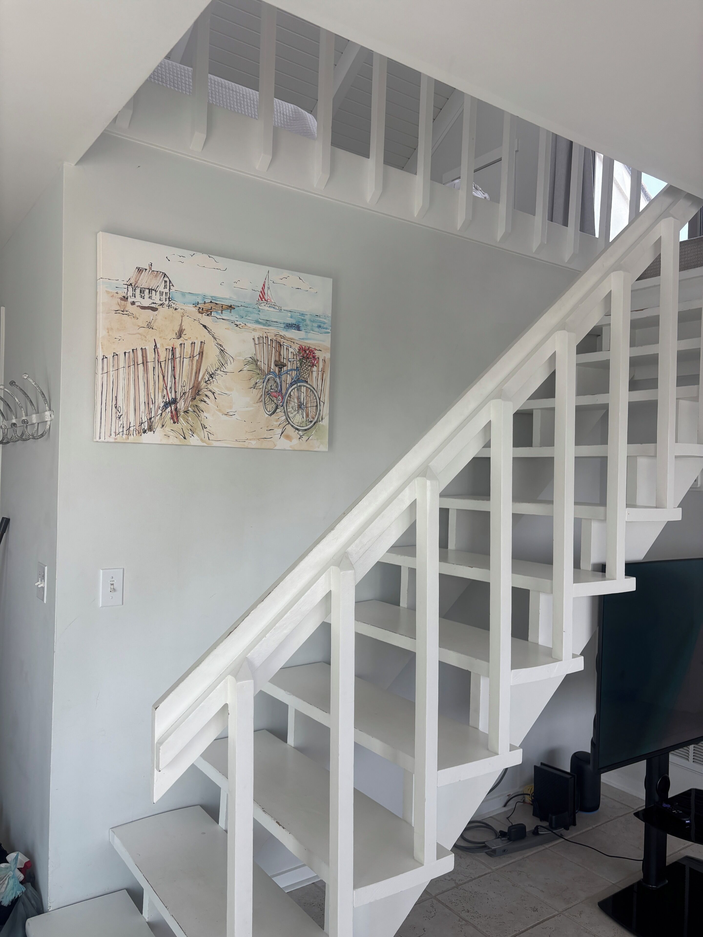 A white staircase with a painting of a beach scene on the wall above.