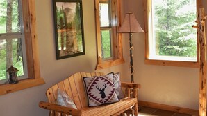 A cozy room with a wooden bench, a lamp, and large windows offering a view of trees.