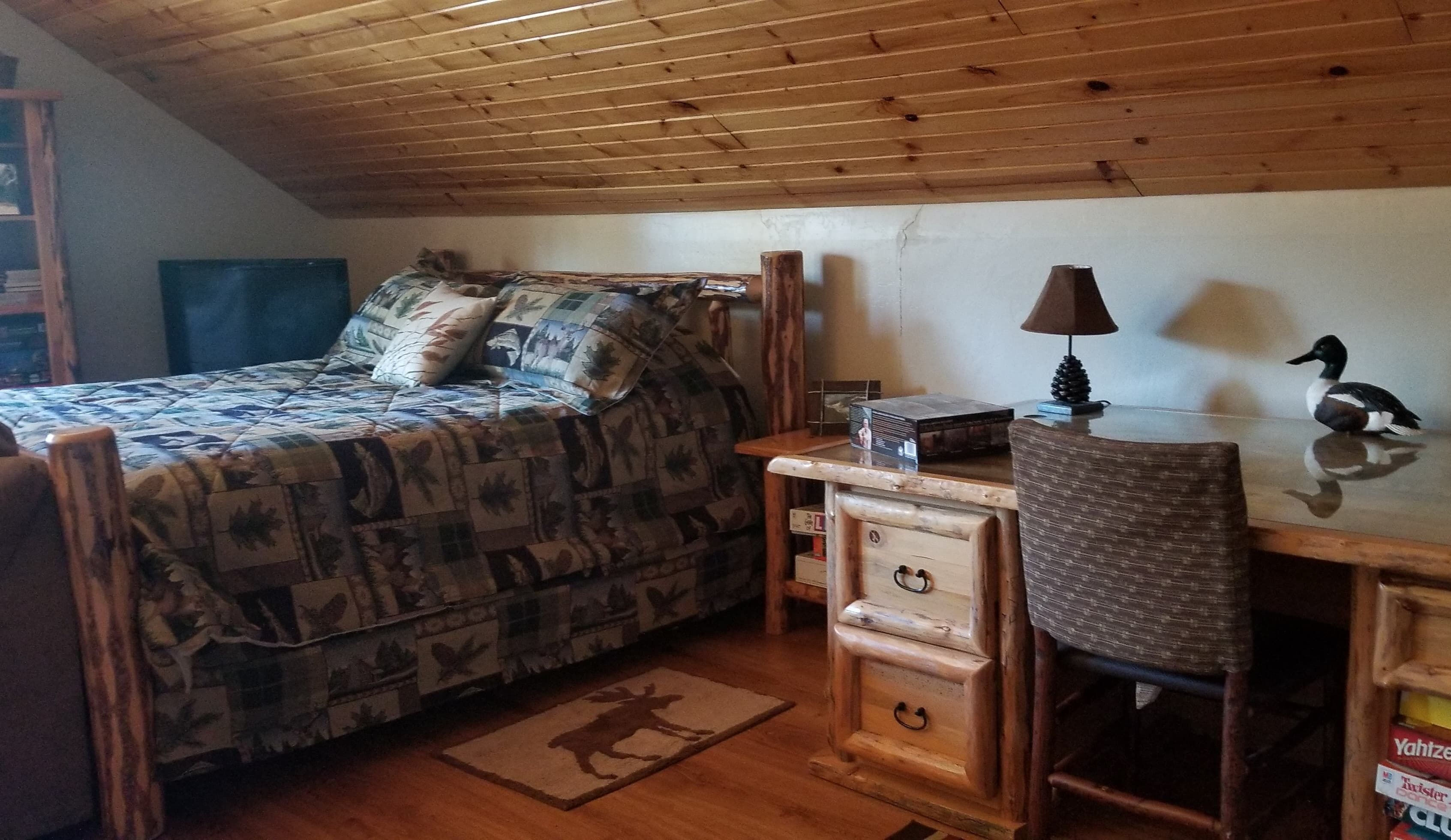 Un dormitorio acogedor con cama, un escritorio de madera, una lámpara y una pequeña mesa con un objeto decorativo.