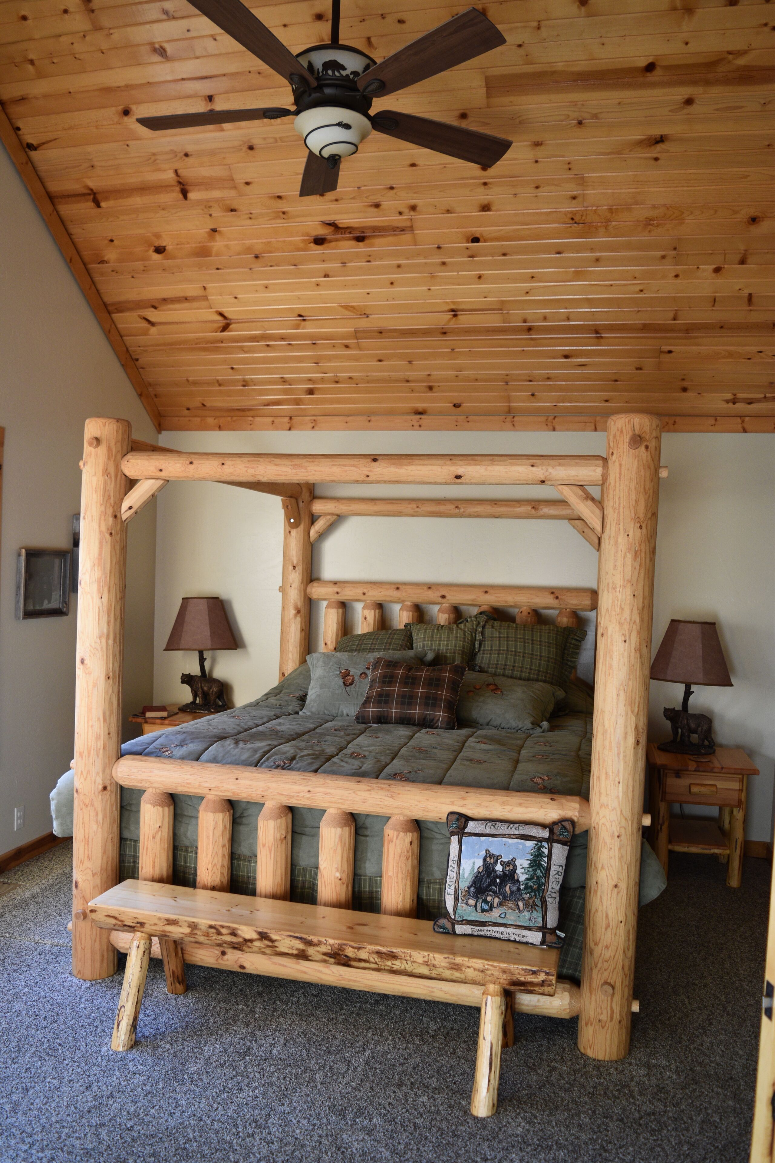 Una cama con dosel de madera, un ventilador de techo, dos mesitas de noche con lámparas y un cuadro enmarcado en la pared.