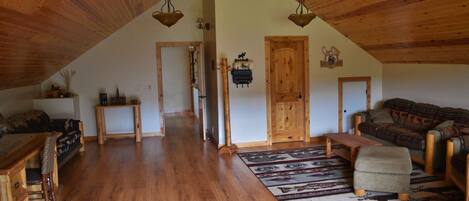 A spacious living area with wooden flooring, a large sofa, a wooden coffee table, and a patterned rug.