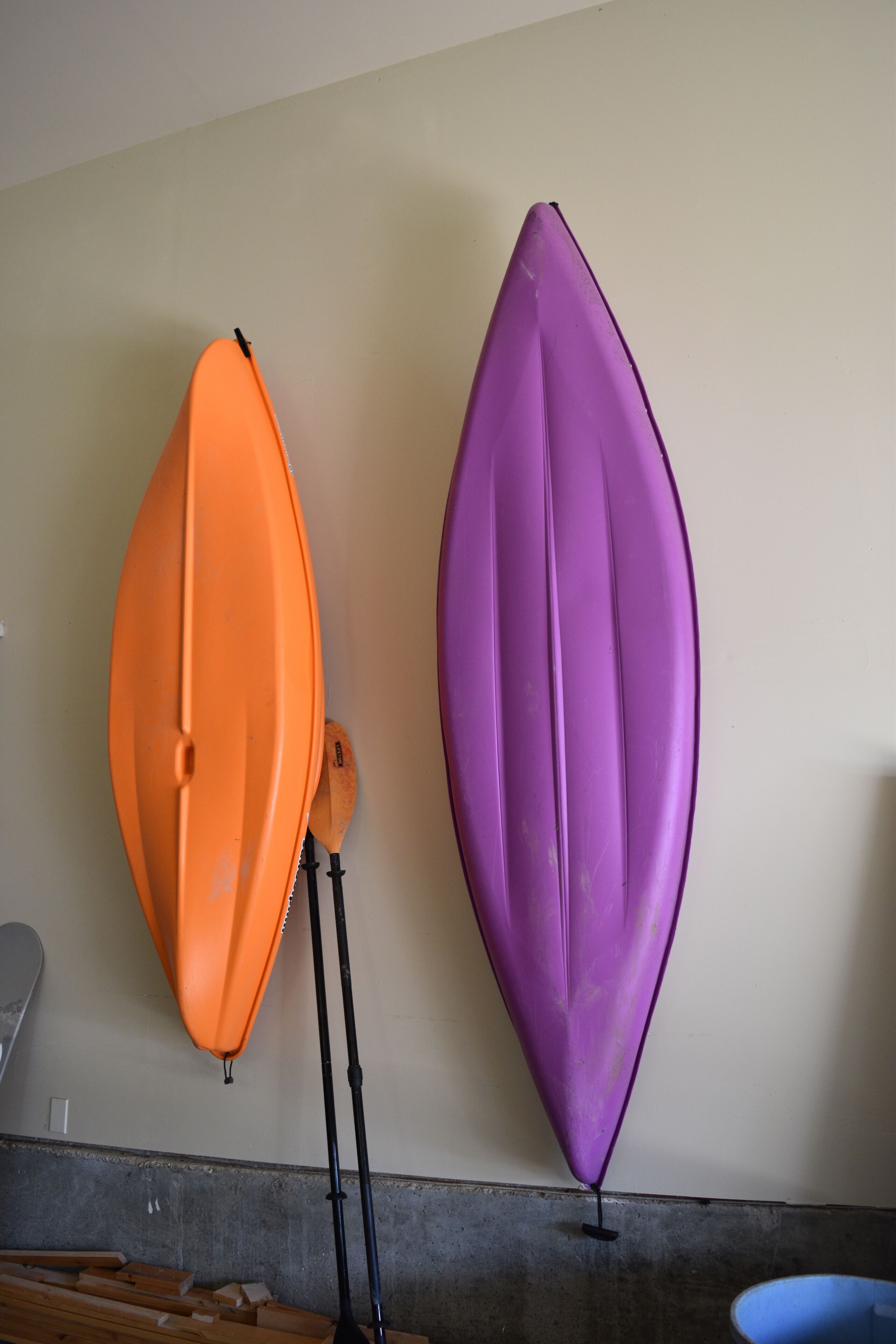 Zwei Kajaks, ein orangefarbener und ein violetter, hängen an einer Wand.