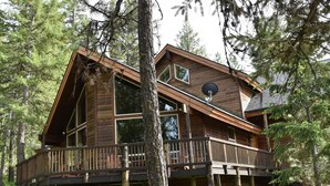 A wooden cabin with a deck, surrounded by trees.